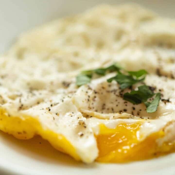 close up of a fried over medium egg topped with fresh basil on a white plate
