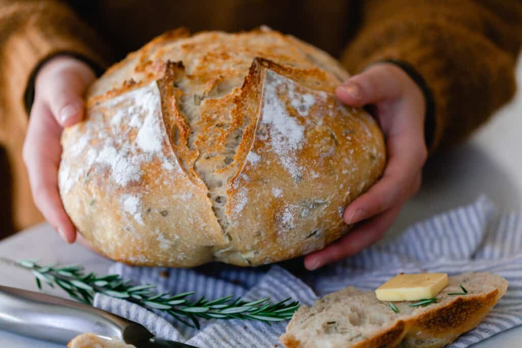 hand holding a loaf of sourdough rosemary bread