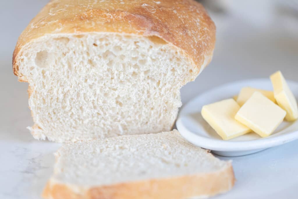 sourdough potato bread with a slice of bread sitting in front of the loaf with a small plate of sliced butter to the left