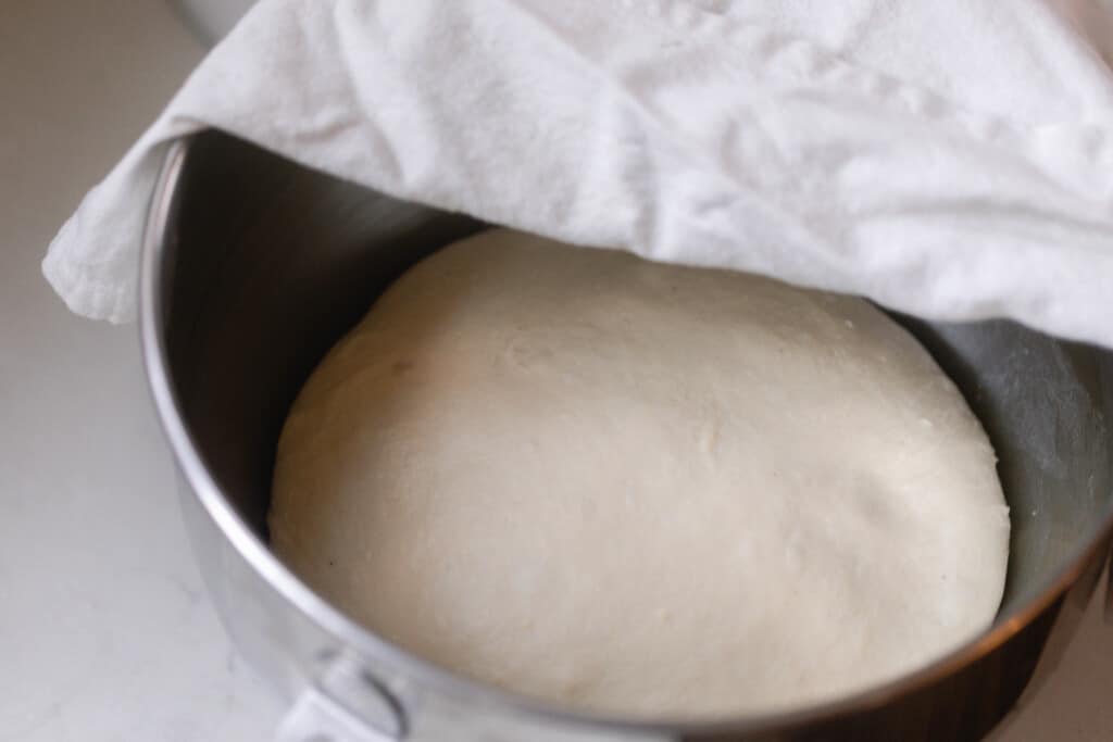 risen dough in a metal stand mixer bowl with a white towel