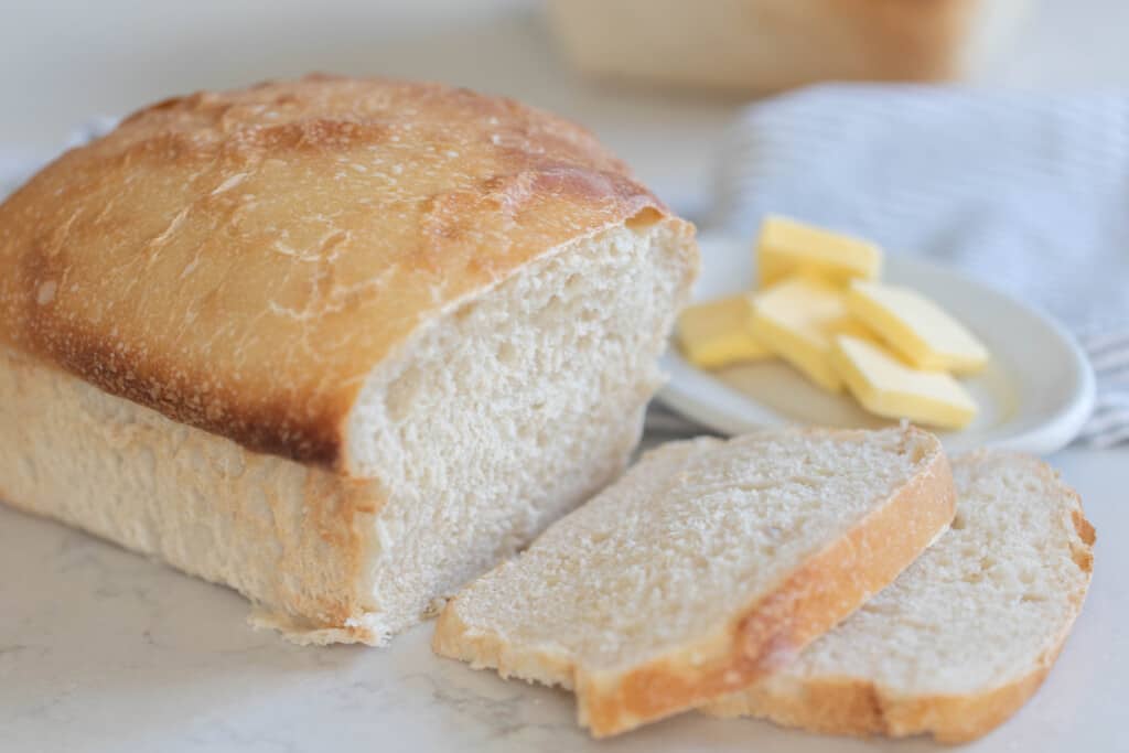 loaf of sourdough potato bread with two slices of bread sliced off the loaf. A small dish of pats of butter behind the loaf