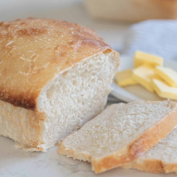 loaf of sourdough potato bread with two slices of bread sliced off the loaf. A small dish of pats of butter behind the loaf