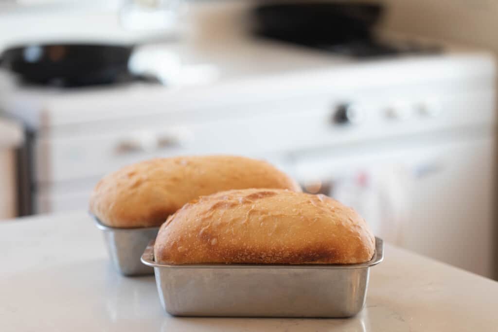 two loaves of sourdough potato bread on a white countertop with vintage white stove in the background