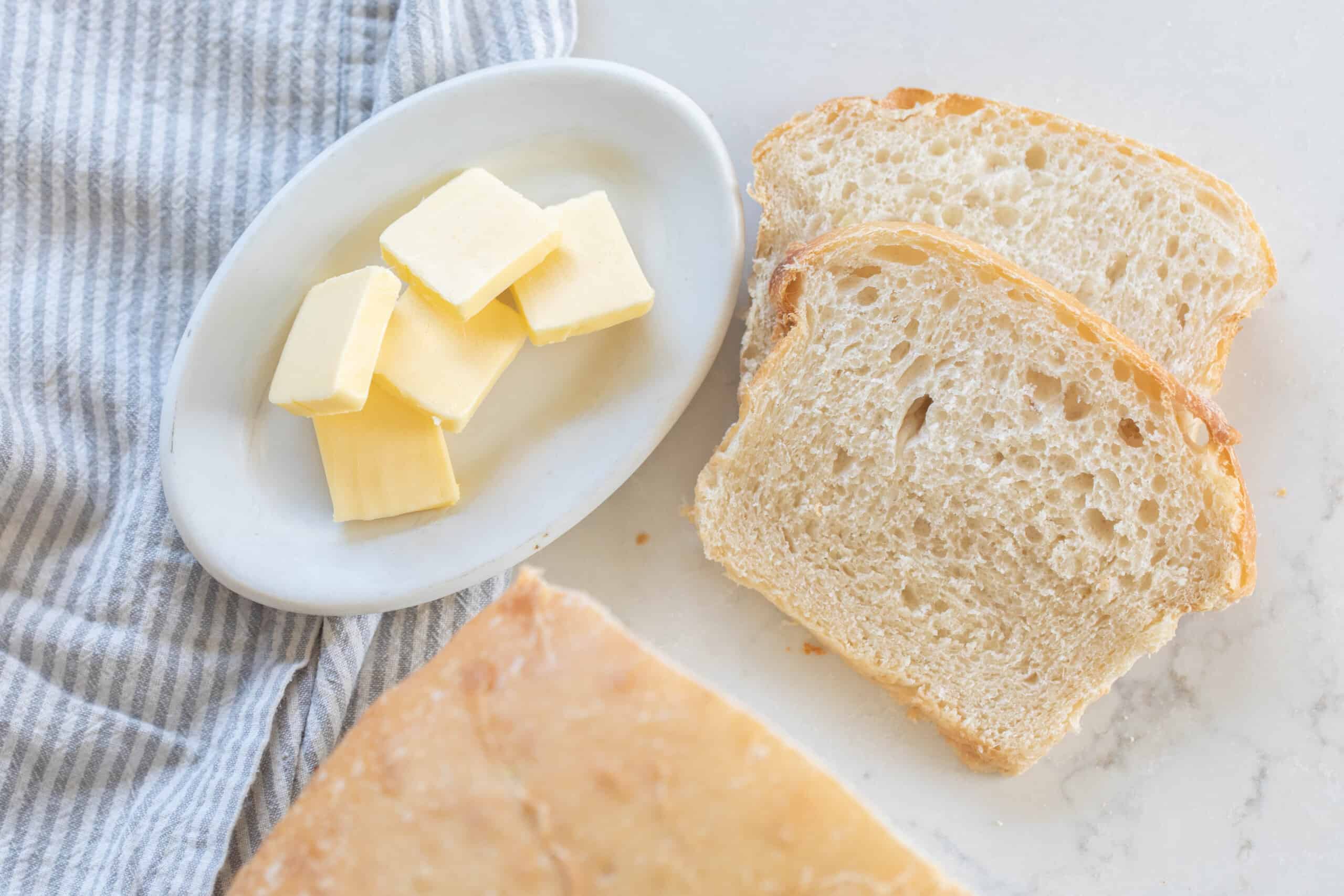 sourdough potato bread sliced on a white countertop with a plate of butter to the left