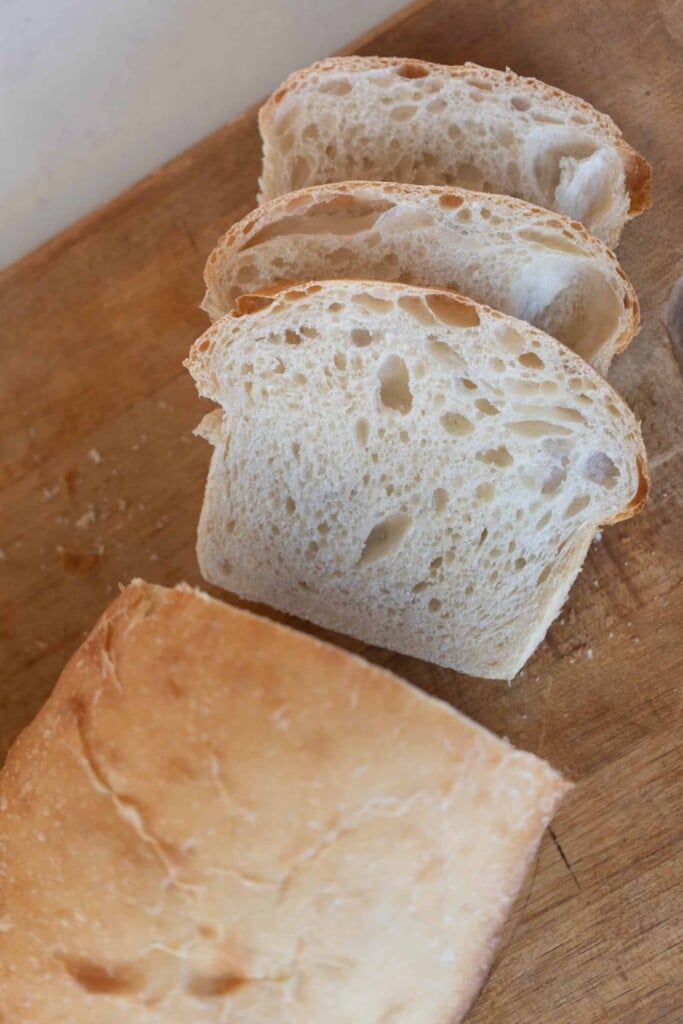 overhead photo of a loaf of sourdough potato bread with three slices of bread laying in front of the loaf on a wood cutting board.