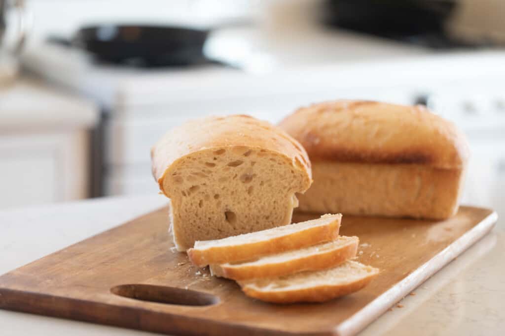 two loaves of sourdough potato bread on a wood cutting board on a white countertop with a vintage stove in the background