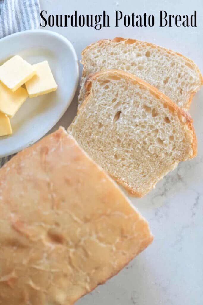 overhead photo of a loaf of sourdough potato bread with two slices laying on a white countertop next to the remaining loaf. A small dish of sliced butter to the left