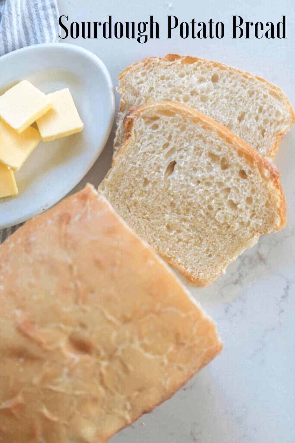 overhead photo of a loaf of sourdough potato bread with two slices laying on a white countertop next to the remaining loaf. A small dish of sliced butter to the left