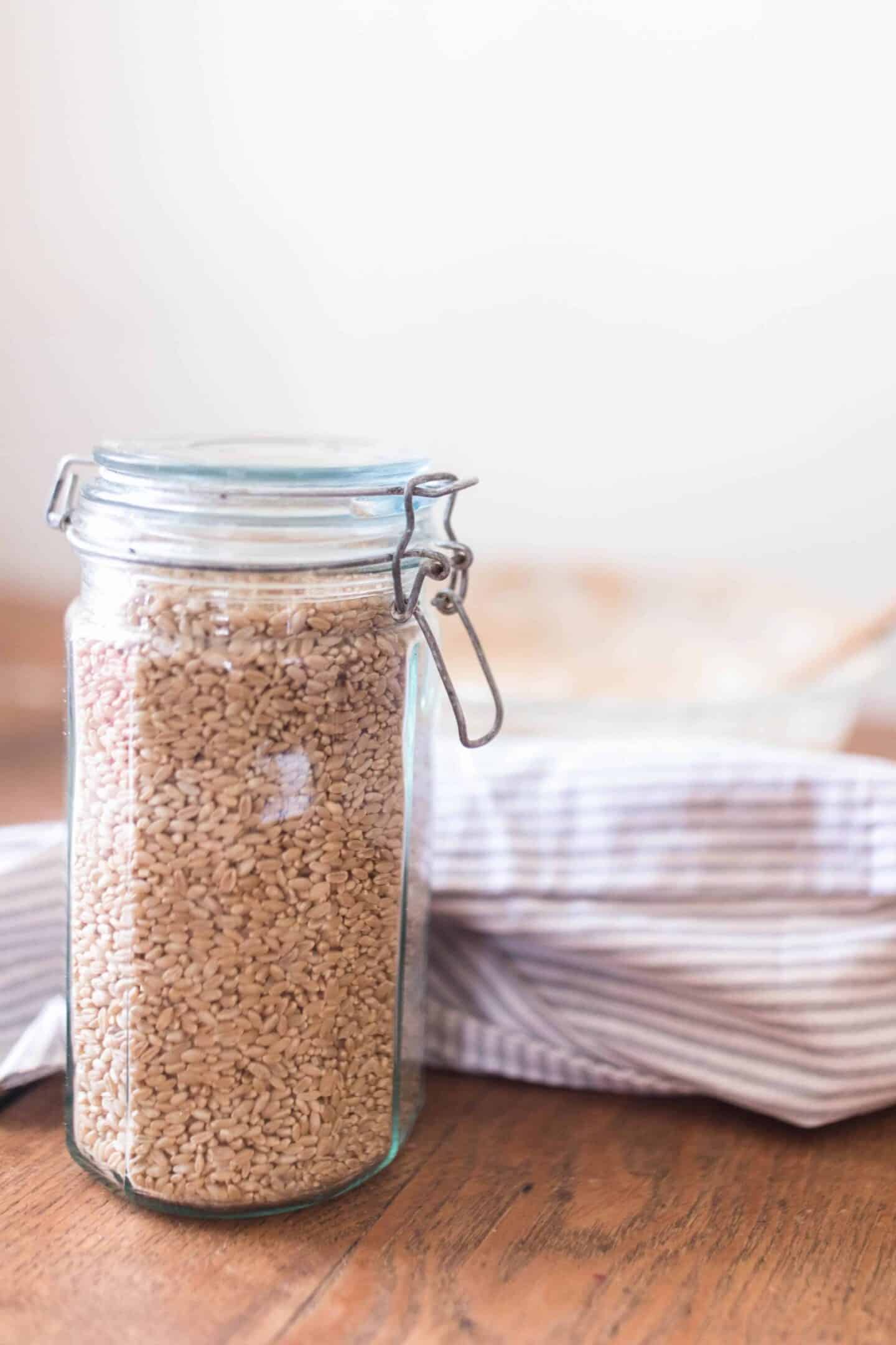 swing top jar full of wheat berries on a wood table with a blue and white towel behind it.