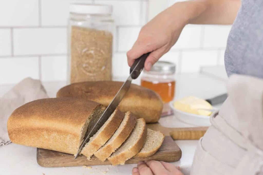 women slicing bread made with fresh milled wheat berries on a wood cutting board