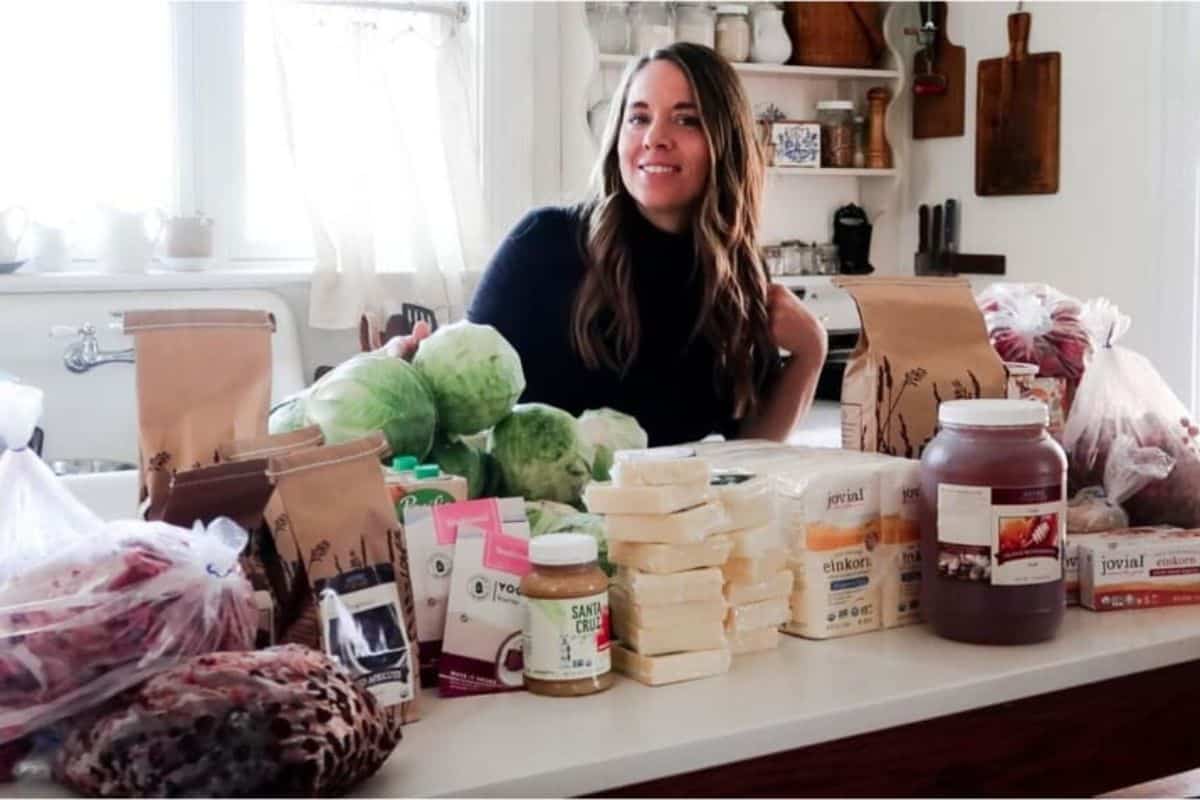 A woman standing behind a kitchen counter full of a bulk order of food. 