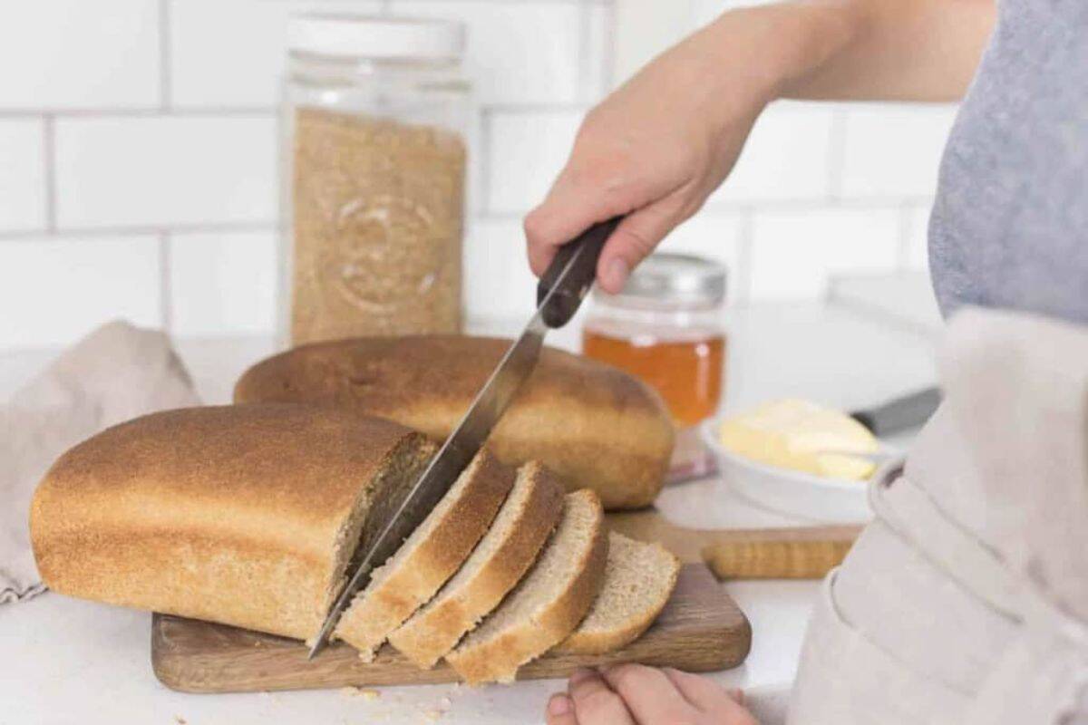 A woman cutting a loaf of bread on a cutting board. 