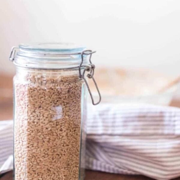 A jar of wheat berries on a wooden countertop next to a blue and white striped tea towel.