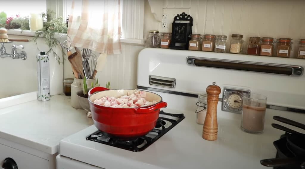 chopped up pork fat in a red cast iron dutch oven on a white vintage stove 