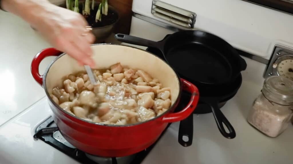 hand stirring a pot of pork fat to make lard on a white vintage stove