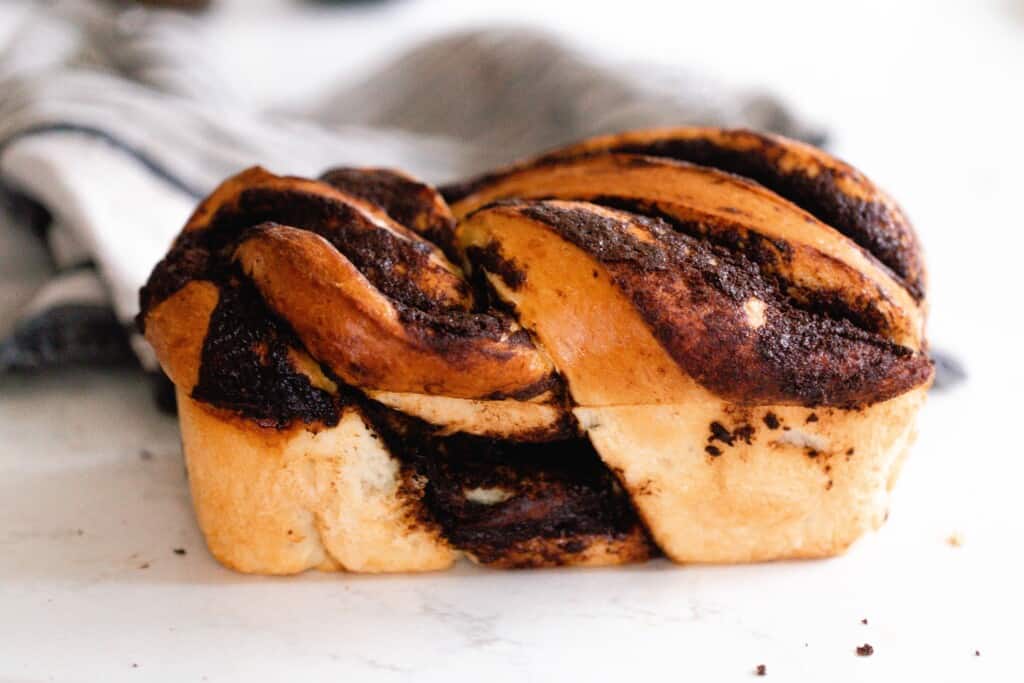 side view of sourdough babka with chocolate filling on a white countertop with a towel in the background