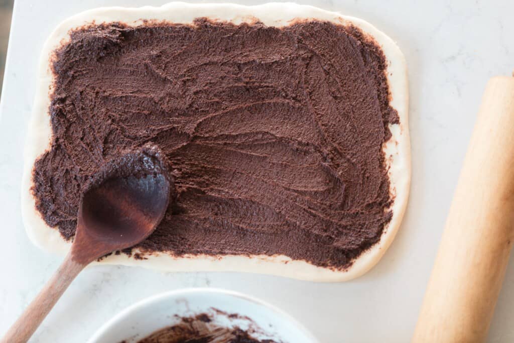 chocolate filling spread out over rolled out brioche bread on a white countertop