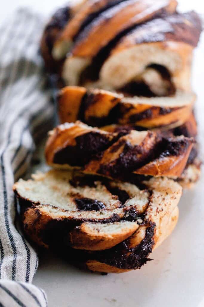sourdough babka with chocolate filling sliced in three thick slices on a white countertop with a black and white towel to the left