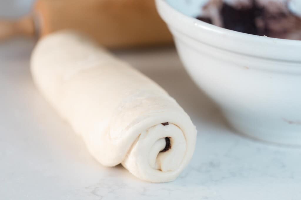 sourdough babka dough rolled up a white countertop. A large bowl with chocolate filling is to the right