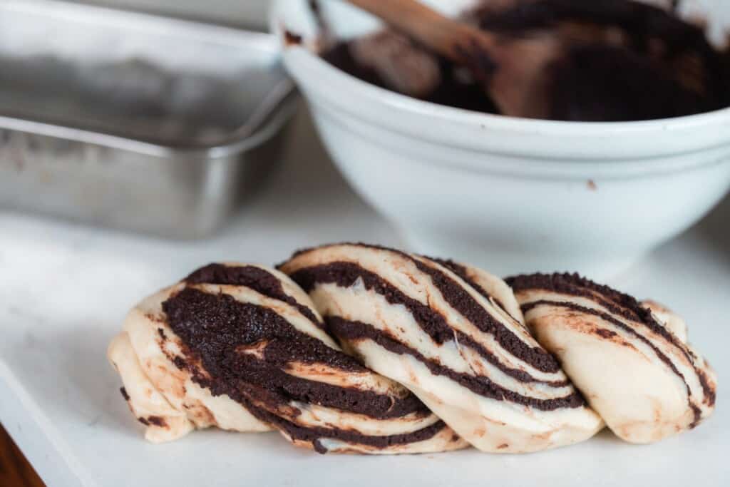 sourdough babka dough with swirls of chocolate filling twisted up on a white countertop.