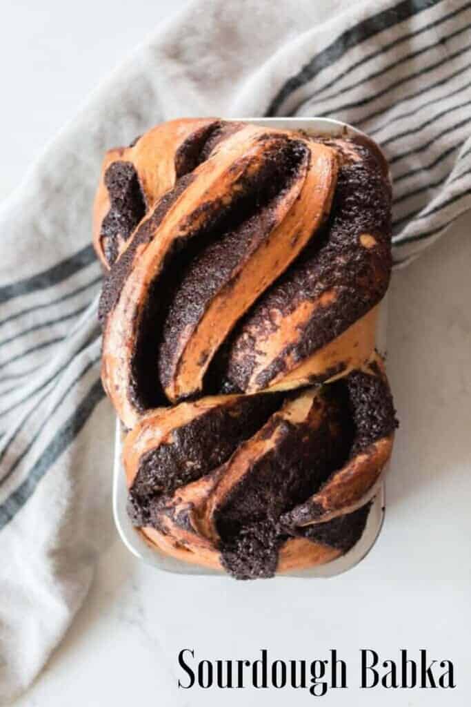 overhead photo of a loaf of sourdough chocolate babka on a white countertop and a black and cream colored stripped towel