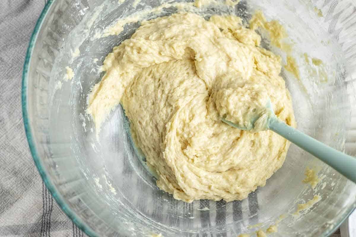 Wet ingredients and dry ingredients being mixed together in a glass bowl with a blue spoon. 