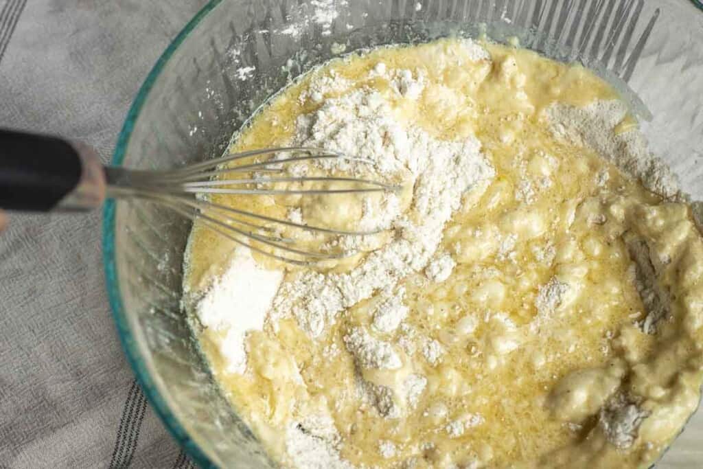 mixing flour, sugar, butter, sourdough starer, and leaveners together in a glass bowl with a whisk