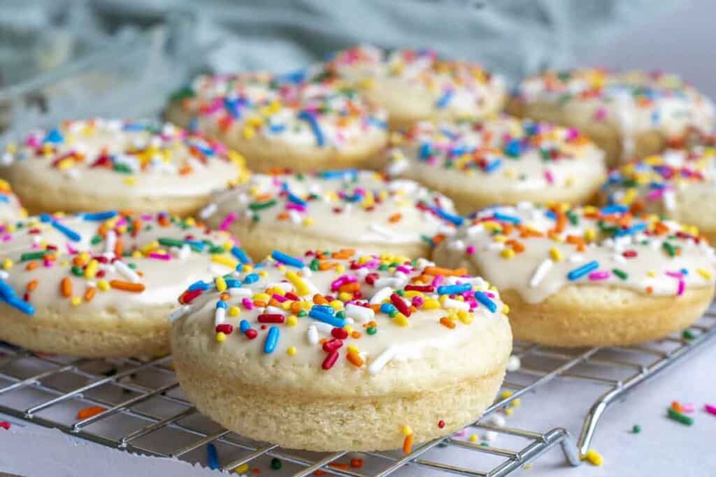 side view of a dozen glazed sourdough donuts with sprinkles on a wire rack