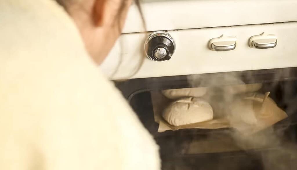 sourdough bread bowls on a baking sheet in an oven with lots of steam