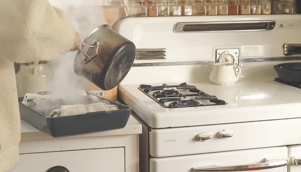 a pot of boiling water being poured over a baking dish full of rolled up towels