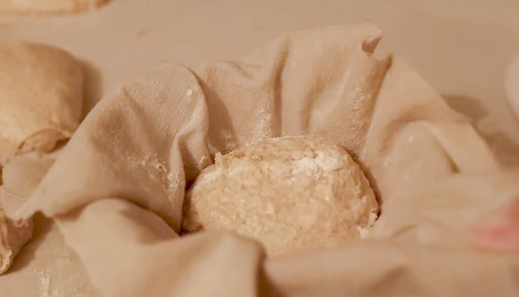 sourdough dough ball in a bowl lined with a tea towel