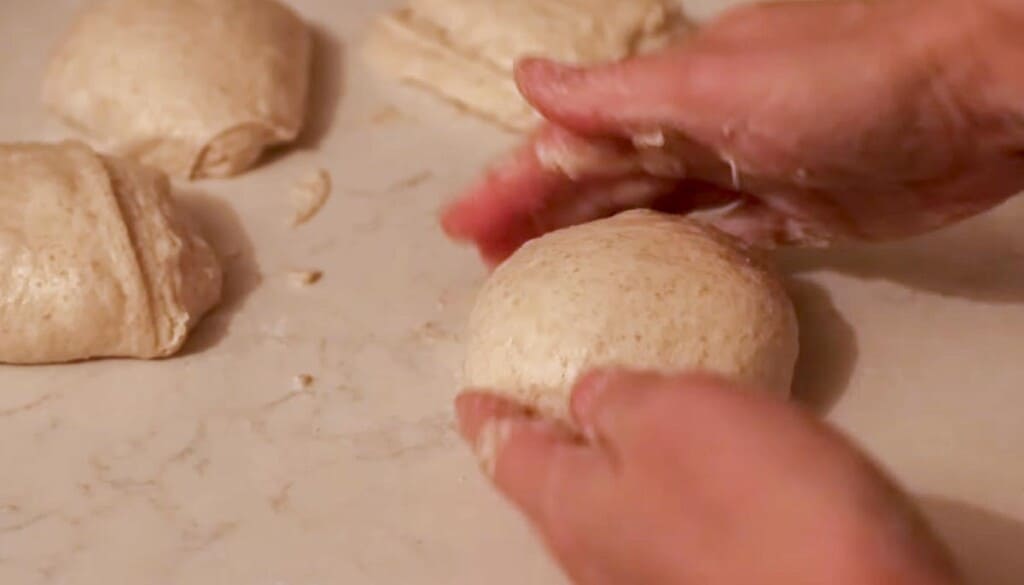 hands shaping small dough balls on a white countertop 