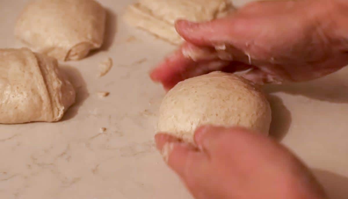 hands shaping small dough balls on a white countertop 