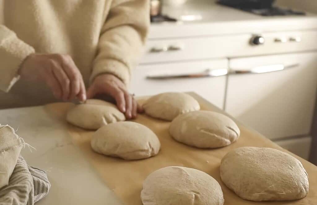 hands scoring the top of sourdough boule dough