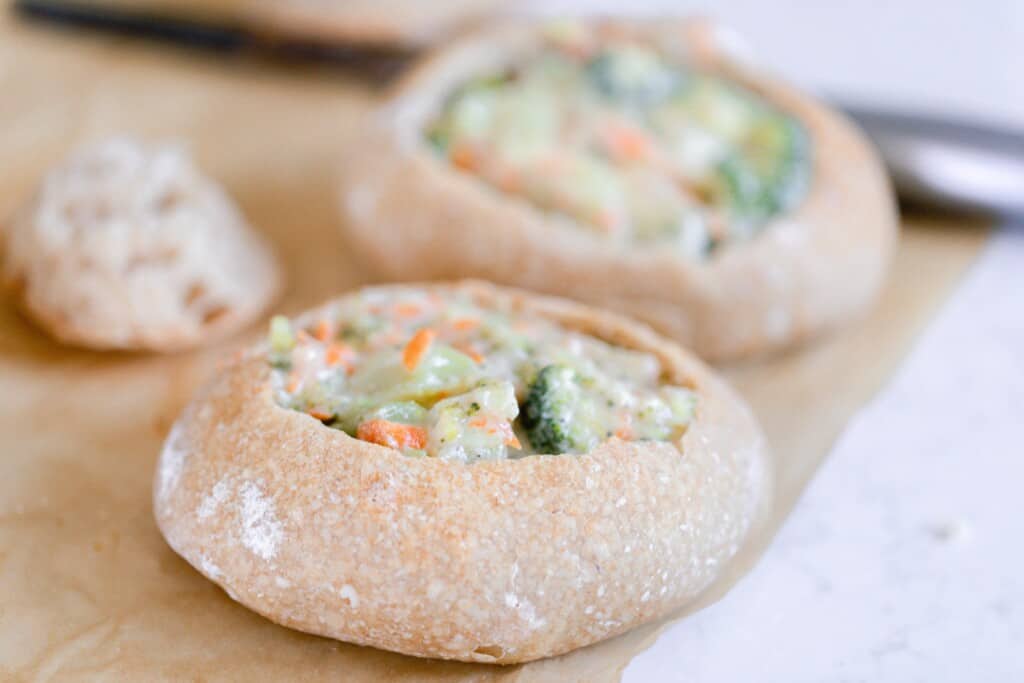 two homemade sourdough bread bowls filled with broccoli cheddar soup sit on parchment paper