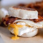 sourdough breakfast sandwich made with sourdough English muffins, thick slices of bacon, cheese, and an over easy egg on parchment paper