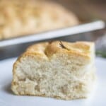 sourdough discard focaccia on a white plate with a tray of more focaccia in the background