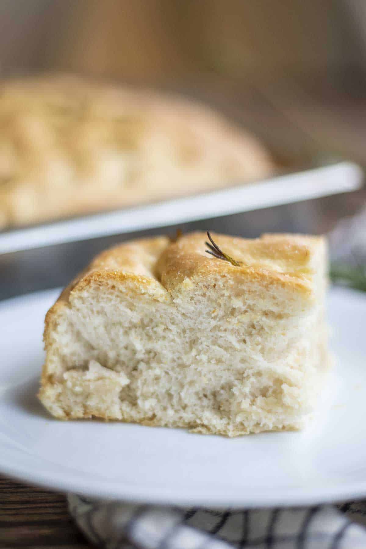 sourdough discard focaccia on a white plate with a tray of more focaccia in the background