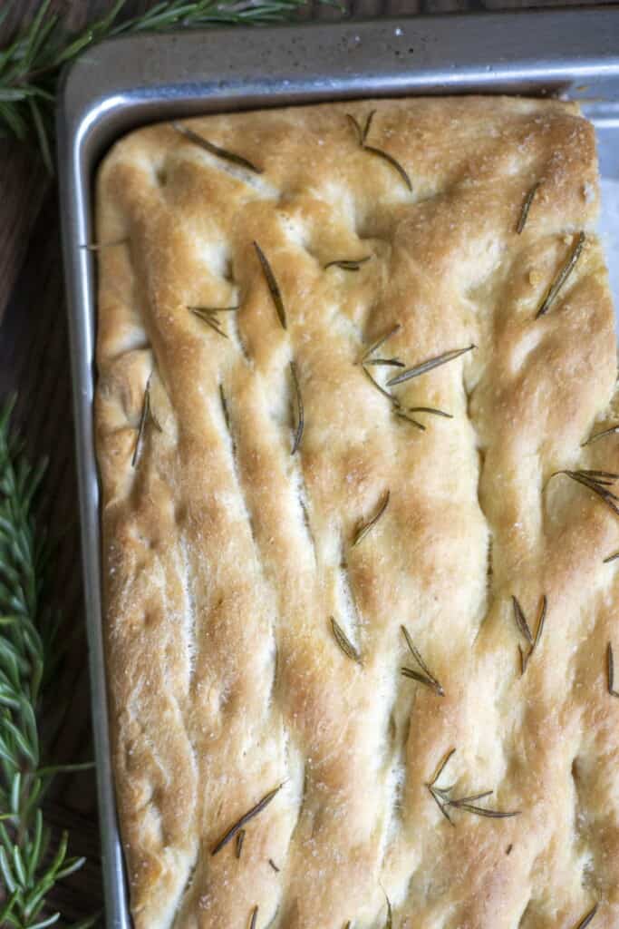overhead picture of sourdough discard focaccia topped with rosemary in a baking sheet