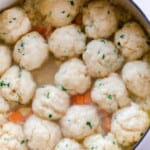 sourdough dumplings simmering in chicken soup in a white dutch oven