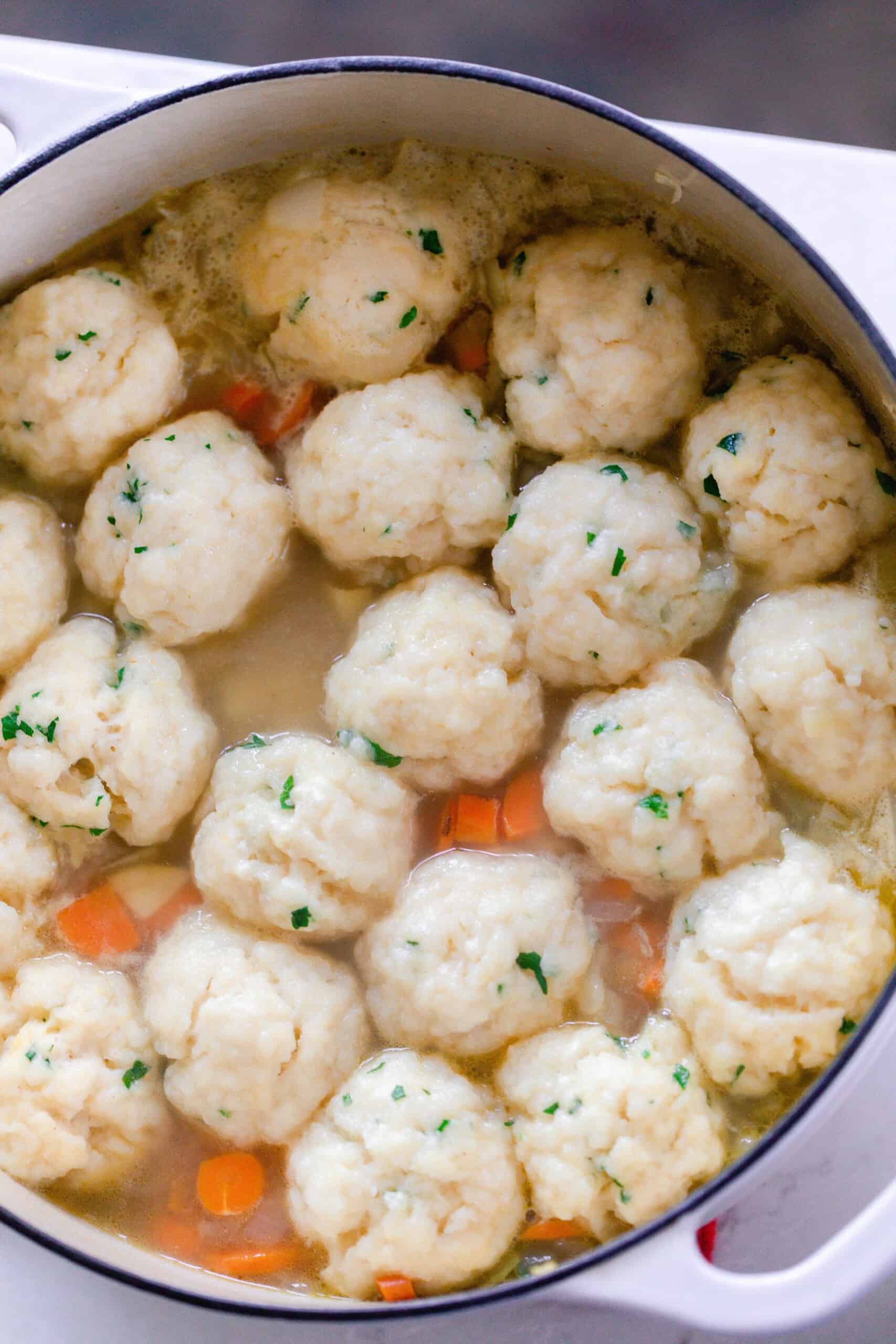 sourdough dumplings simmering in chicken soup in a white dutch oven