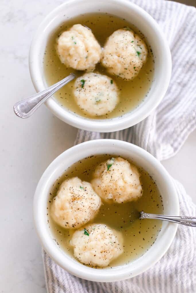 overhead photo of two white bowls full of chicken soup with sourdough dumplings. The bowls sit on a gray and white tea towel