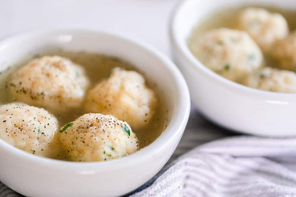 two white bowls full of sourdough chicken and dumplings on a white countertop with a gray and white striped tea towel to the side