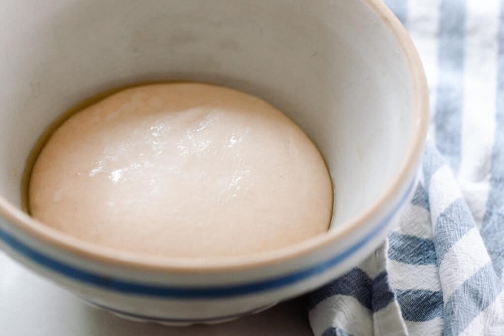 dough in cream and blue stoneware bowl on a white and blue stripped towel