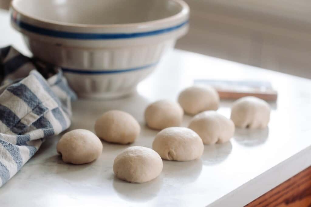 8 balls on dough on a white quartz countertop next to a towel and ironstone bowl