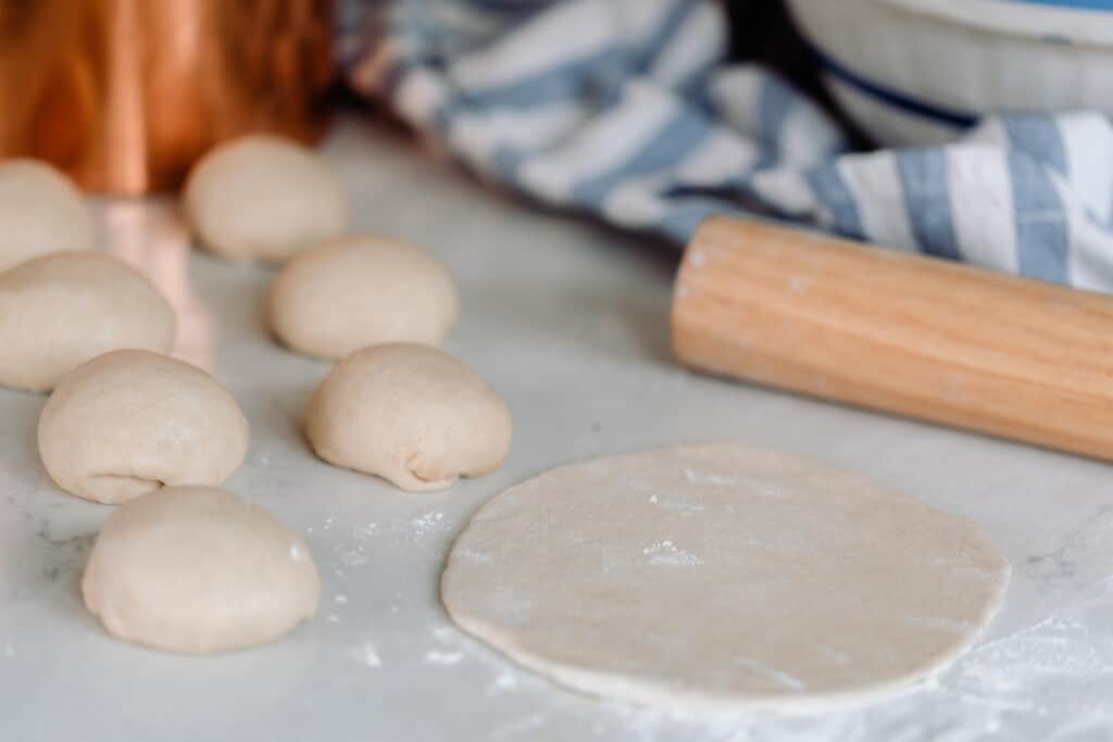 rolling pin rolling out pita dough into round circles on a white quartz countertop 