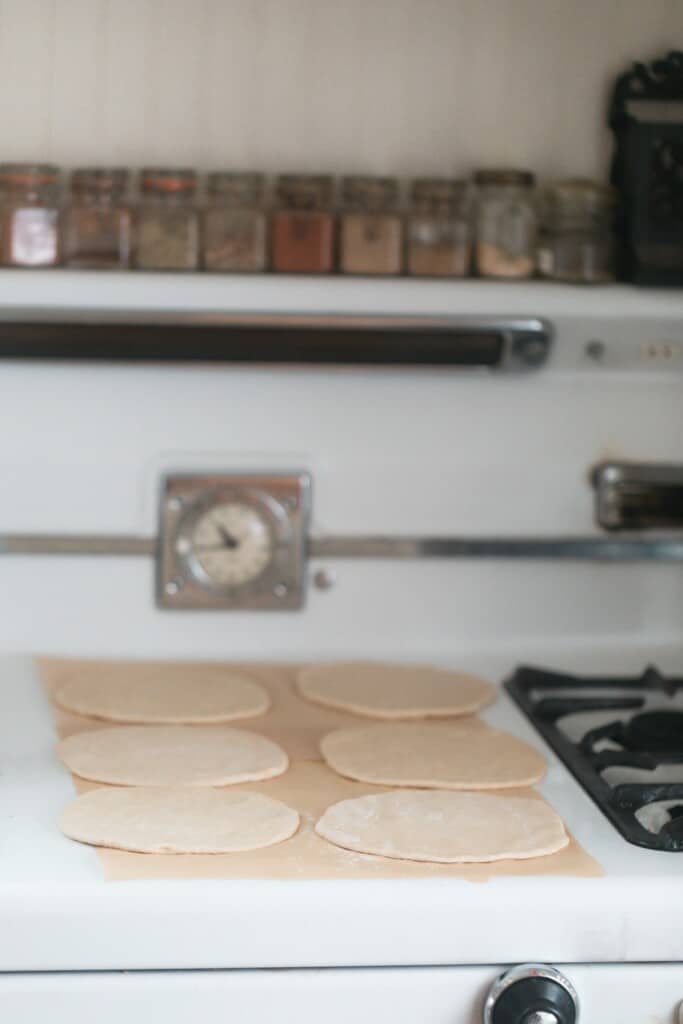 sourdough pita bread dough rolled out on parchment paper on a white vintage stove