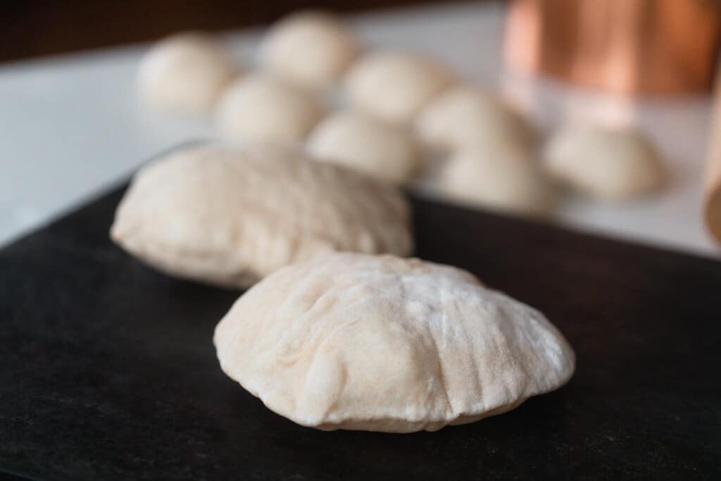 sourdough pita bread cooking on a pizza stone with more balls of dough in the background