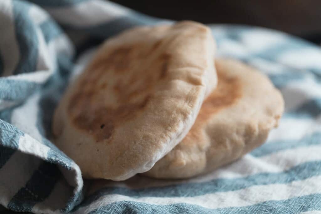 close up of two sourdough pita breads on a white and blue stripped towels