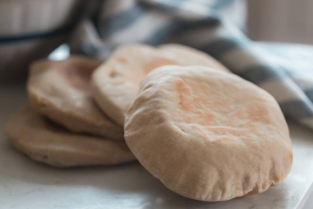 four sourdough pita breads on a white counter with a blue and white stripped towel in the background